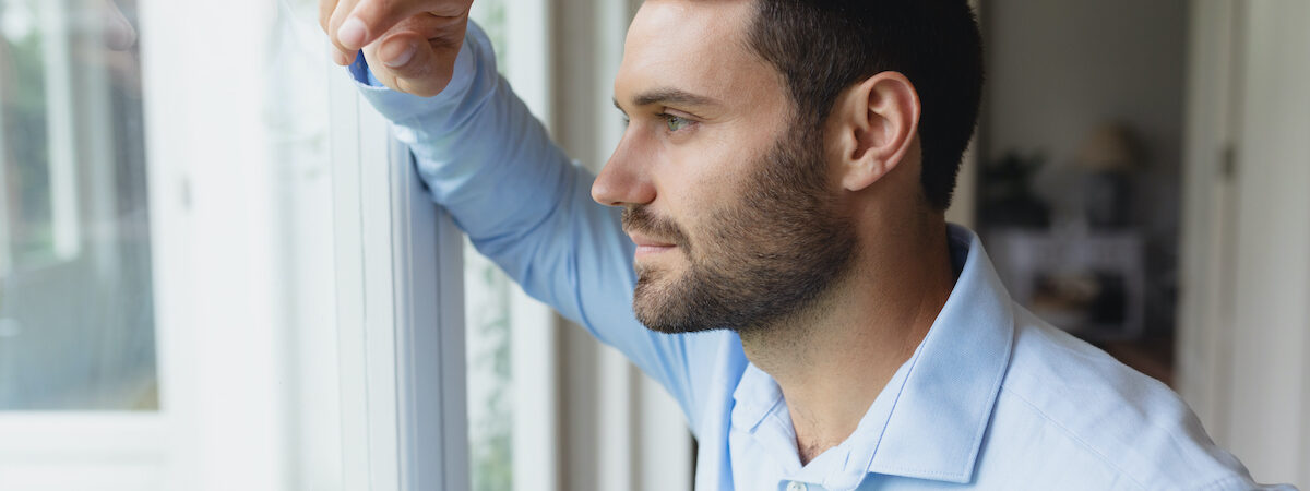 Side view of thoughtful Caucasian man looking outside through window in a comfortable home