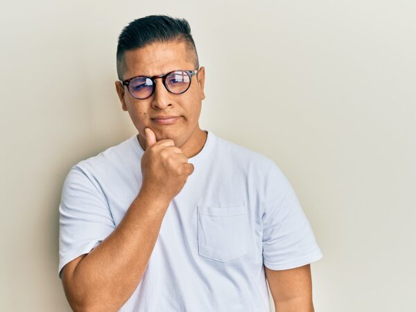 Young latin man wearing casual clothes and glasses thinking concentrated about doubt with finger on