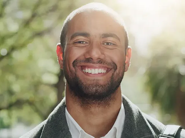 Smiling man outdoors in dappled sunlight among trees