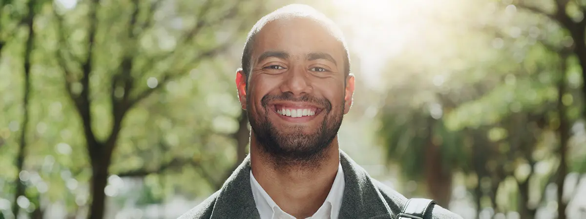 Smiling man outdoors in dappled sunlight among trees