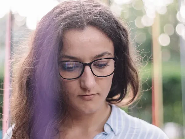 Pensive woman with glasses outdoors, looking down thoughtfully
