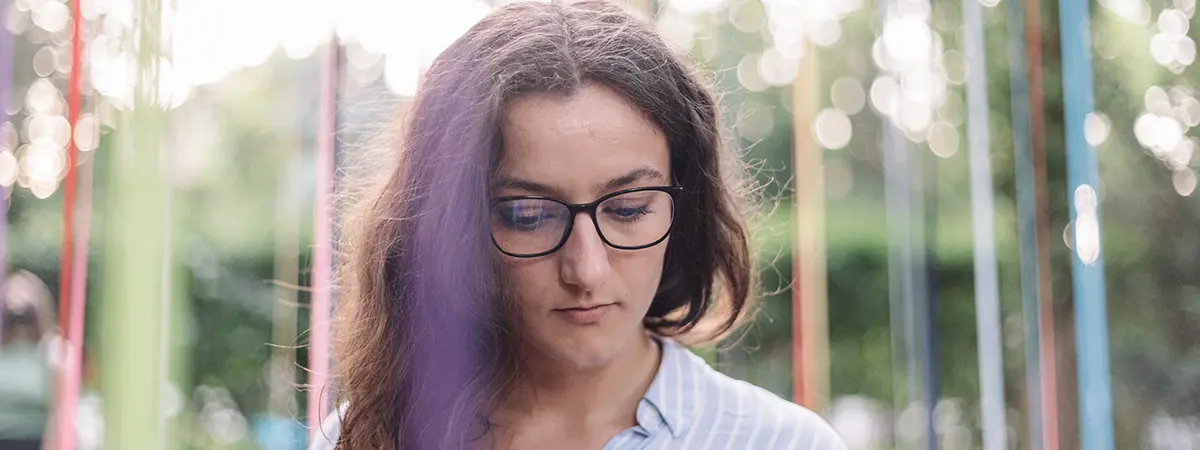 Pensive woman with glasses outdoors, looking down thoughtfully